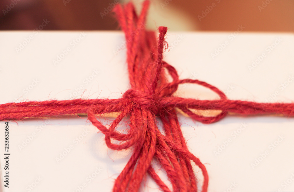 Close-up: white box with a gift is well tied with red tape. Concept: time to give and receive gifts. 