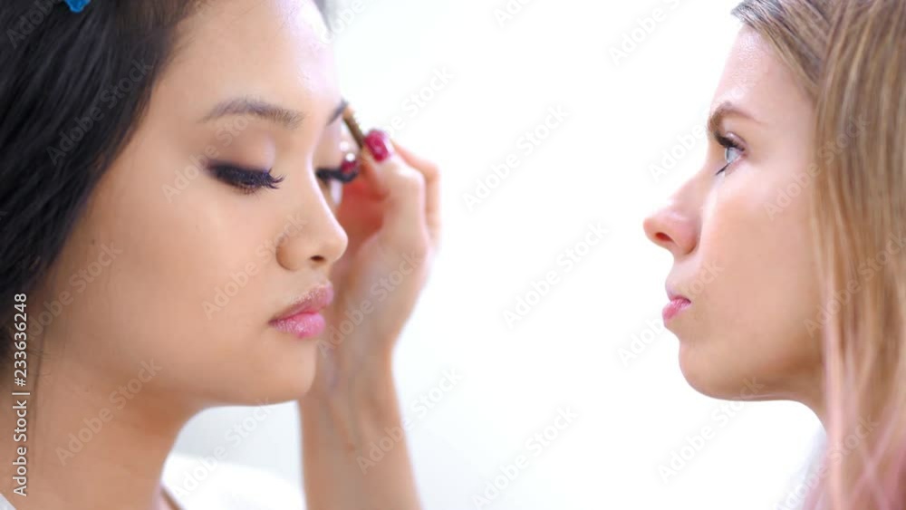 Side view professional make-up artist creating perfect shape of eyebrow for attractive client Side view professional make-up artist creating perfect shape of eyebrow for attractive client
