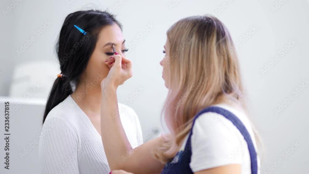 Professional female make-up artist making makeup eyebrows of woman model using pencil medium shot Professional female make-up artist making makeup eyebrows of woman model using pencil medium shot