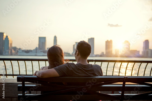 Photography Rear view of couple sitting on bench while looking at river in city