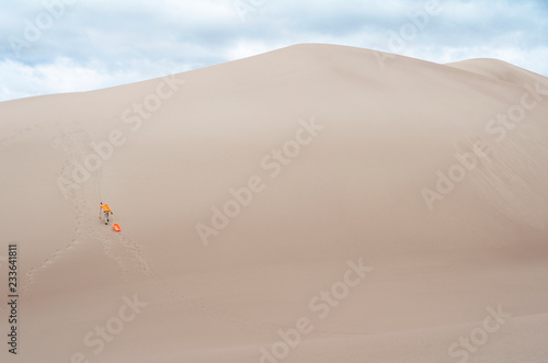 Rear view of hiker with poles and sled walking on sand dune