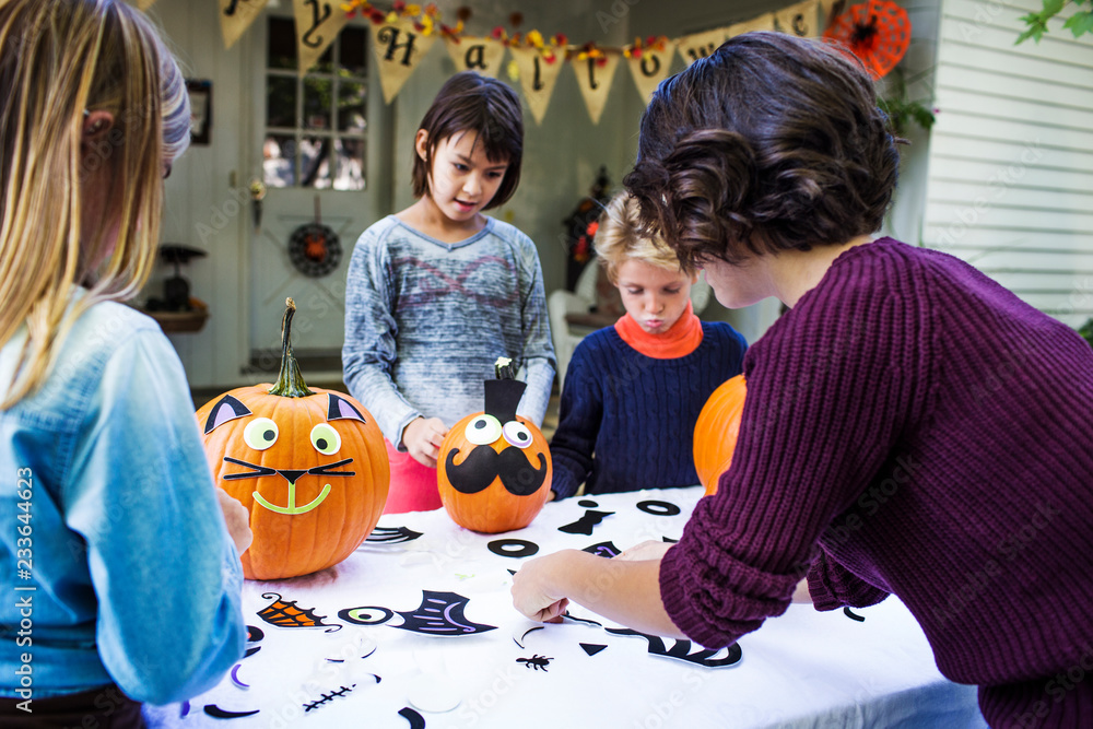 Obraz premium Mother assisting children in decorating pumpkins at table during Halloween party