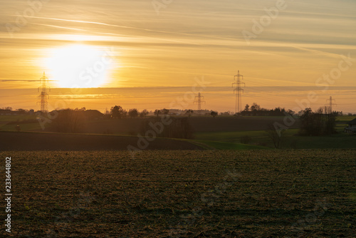 Sonnenuntergang mit Strommasten im Vordergrund Ackerland