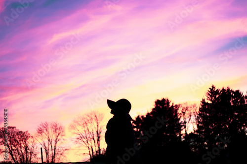 purple sky and silhouettes of a woman with hat and trees