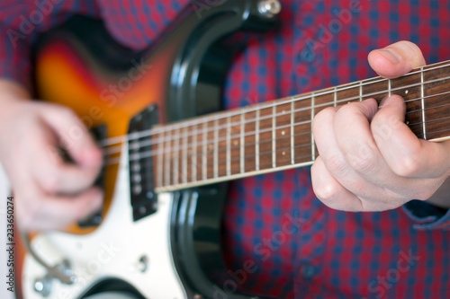 Hands of a man in a plaid shirt playing vintage sunburst guitar