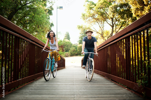 Tablou pe pânză Couple riding bicycle on footbridge at park