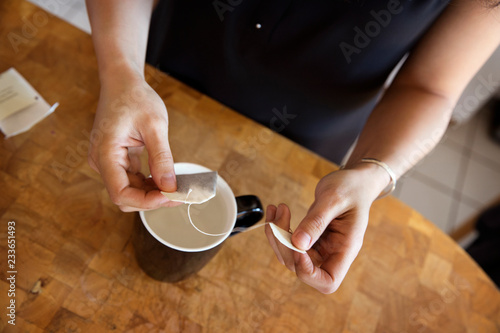 Midsection of woman holding teabag over mug at kitchen counter