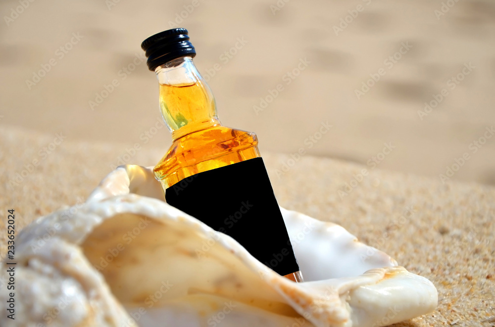 little bottles whiskey in the big ocean shell stand on the sand closeup