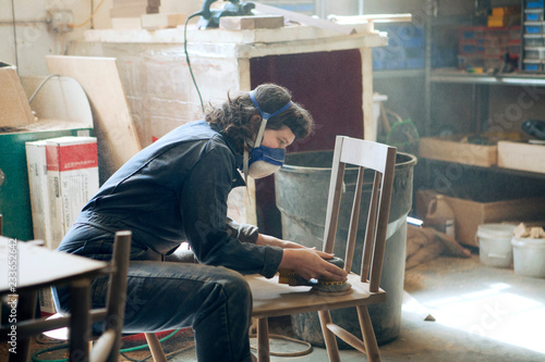 Fotografia Side view of female carpenter sanding wooden chair at workshop