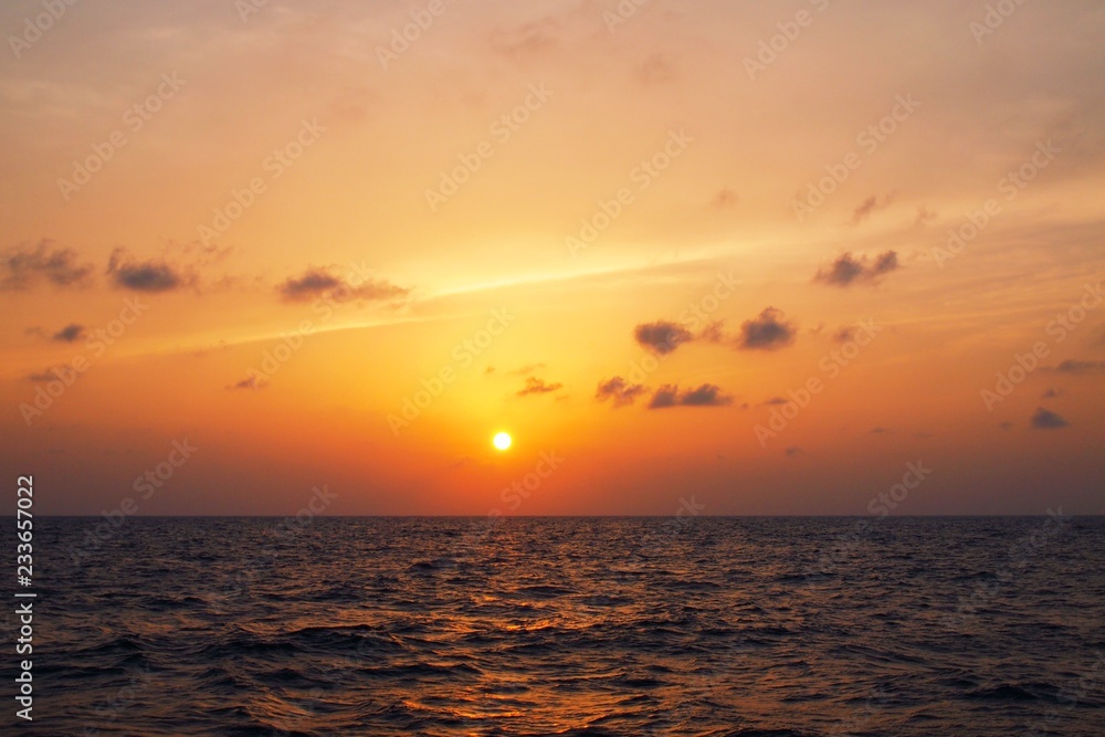 Golden sunset over sea horizon with clouds and light streak over sky during dusk and choppy waves