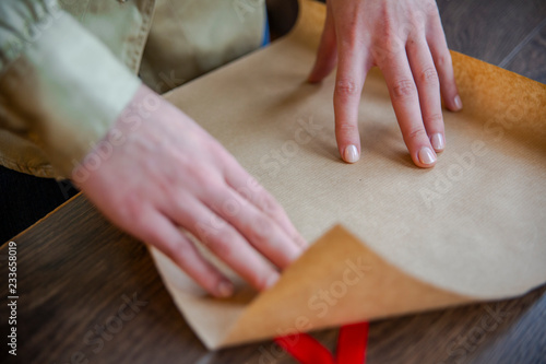 Hands of beautiful young woman wrapping present in brown paper 