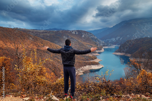 Back view of young man standing with raised hands and looking at lake