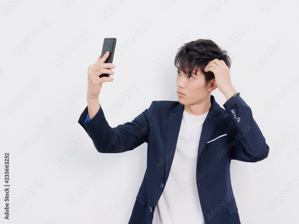 Portrait of handsome Chinese young man in dark blue leisure suit posing against white wall background. Holding mobile phone and taking selfie. Portrait of handsome Chinese young man in dark blue leisure suit posing against white wall background. Holding mobile phone and taking selfie.