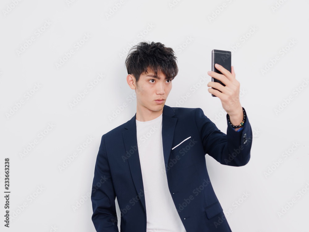 Portrait of handsome Chinese young man in dark blue leisure suit posing against white wall background. Holding mobile phone and taking selfie. Portrait of handsome Chinese young man in dark blue leisure suit posing against white wall background. Holding mobile phone and taking selfie.