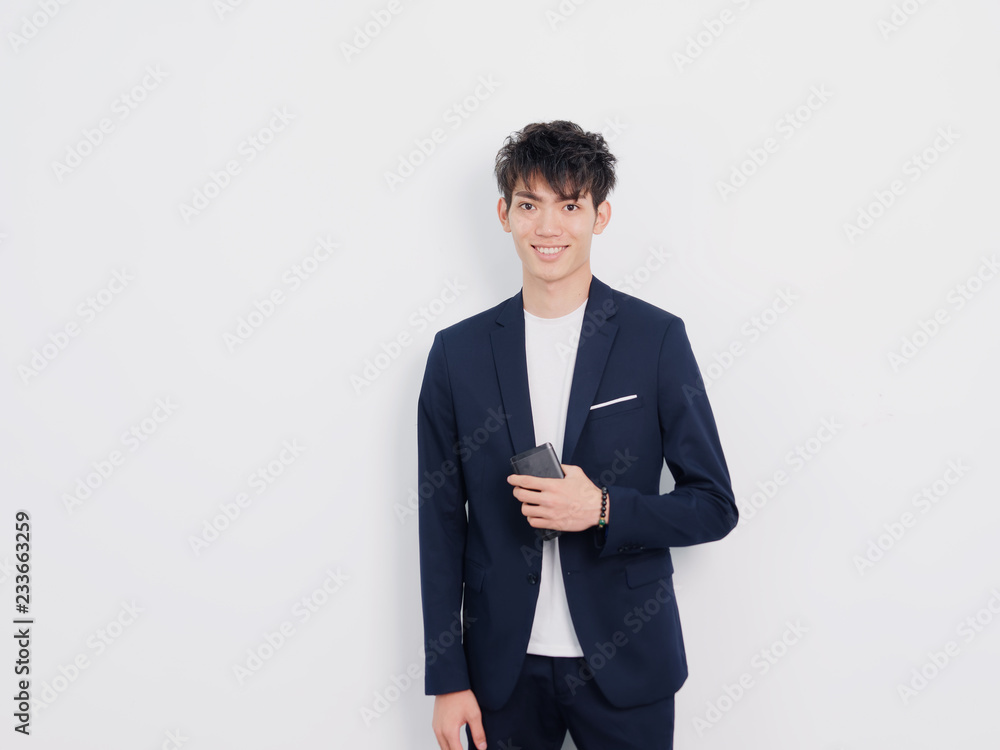 Portrait of handsome Chinese young man in dark blue leisure suit posing against white wall background. Smiling at camera with mobile phone in hand. Portrait of handsome Chinese young man in dark blue leisure suit posing against white wall background. Smiling at camera with mobile phone in hand.