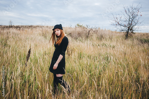 beautiful red-haired woman in a black dress walks on an autumn field. © Денис Кипкаев