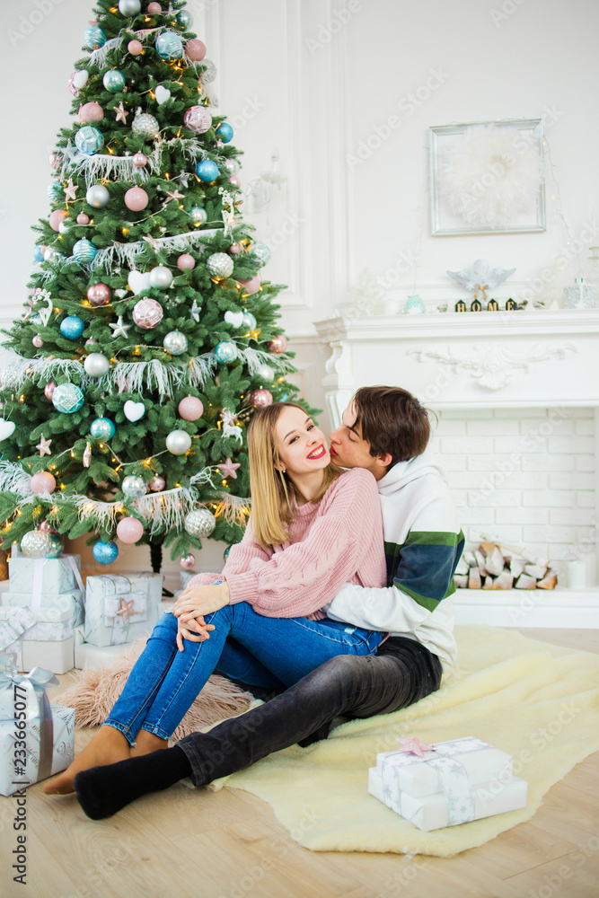 Sweet couple sitting near to a Christmas tree embracing each other Sweet couple sitting near to a Christmas tree embracing each other