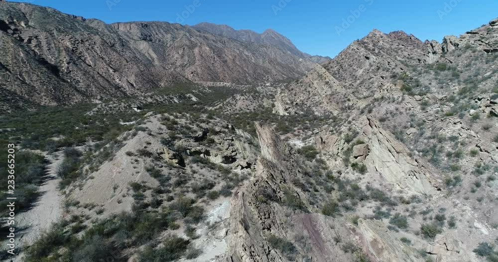 Aerial drone scene of dry valley and folded mountains. Flying above rock formations that emerge from earth with angle. Scarce native vegetation covers low regions. San Juan province, Huaco, Argentina Aerial drone scene of dry valley and folded mountains. Flying above rock formations that emerge from earth with angle. Scarce native vegetation covers low regions. San Juan province, Huaco, Argentina
