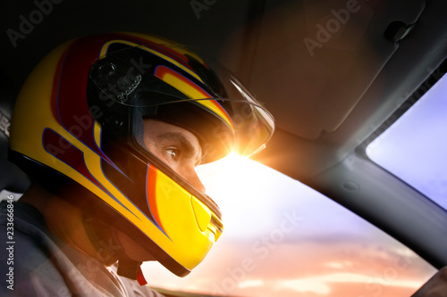 Low angle close-up of man wearing helmet sitting in car at race during sunset