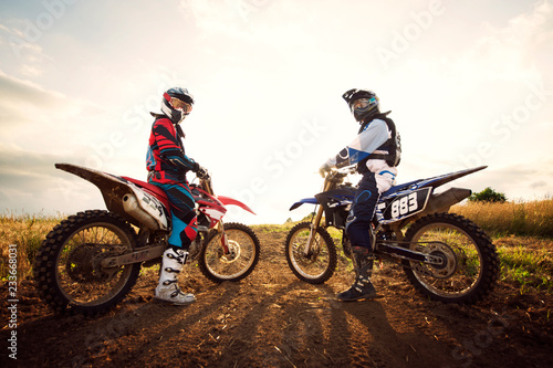 Фотография Side view portrait of dirt bikers sitting on motorcycles at field against sky