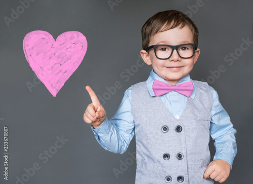 Little boy points at a valentines heart and thinks of love, isolated on gray background