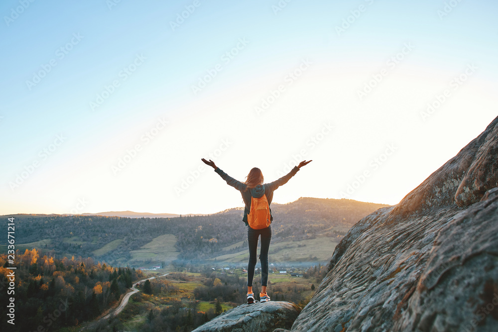 woman hiker with backpack stands on edge of cliff against background of sunrise. Woman is meditation and greeting a sun woman hiker with backpack stands on edge of cliff against background of sunrise. Woman is meditation and greeting a sun