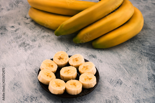 Round sliced banana slices on a round plate, whole fruits on a wooden background.