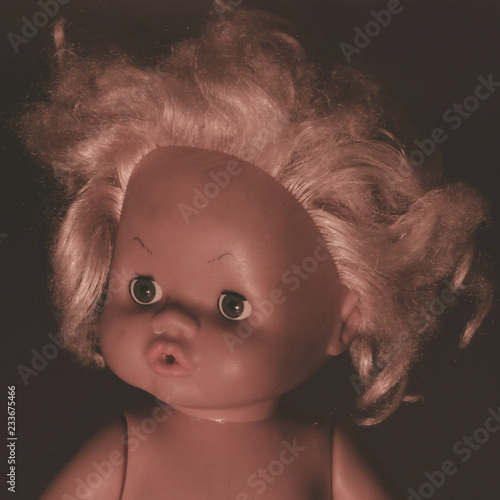 Portrait of an old doll. Plastic doll face in darkness.
