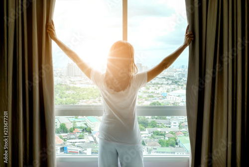 Morning of a new day woman wake up in the bedroom with her refreshing. She stand at the window , raised her two arms and look city view get sunlight