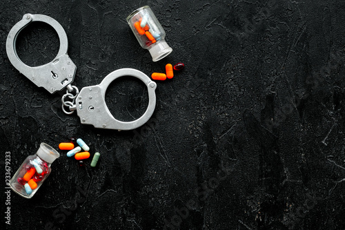 Arrest for illegal purchase, possession and sale drugs concept. Drugs as pills near handcuff on black background top view copy space