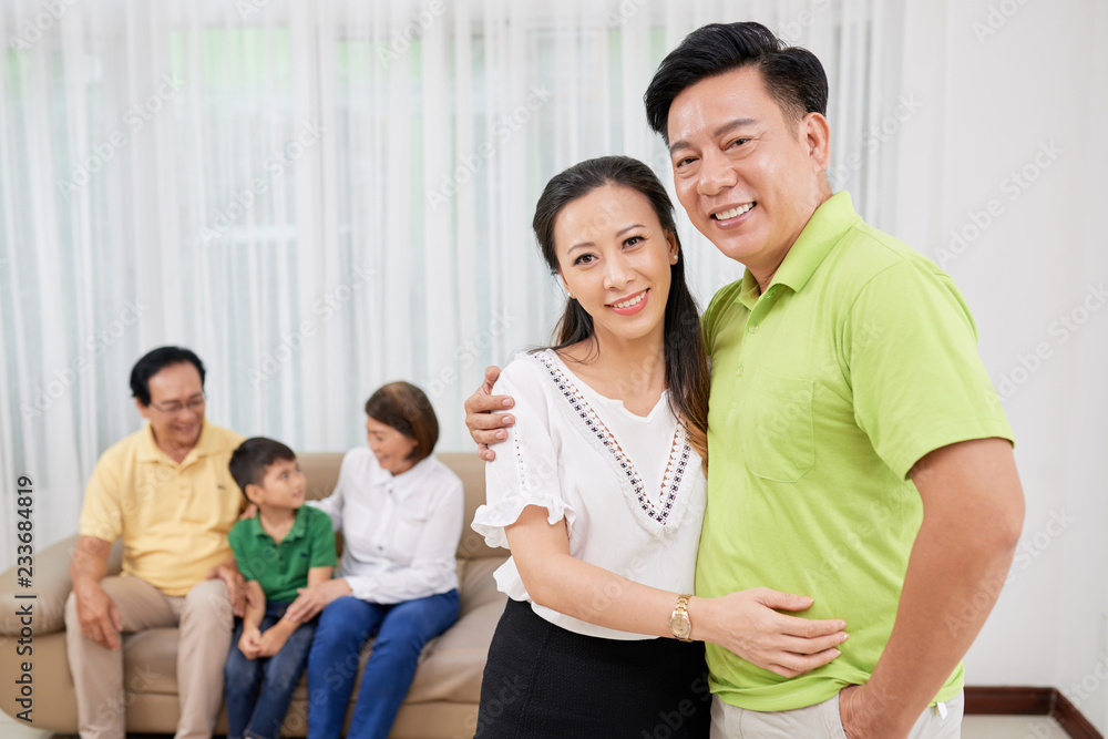 Hugging happy mature Asian couple, their big family in background Hugging happy mature Asian couple, their big family in background
