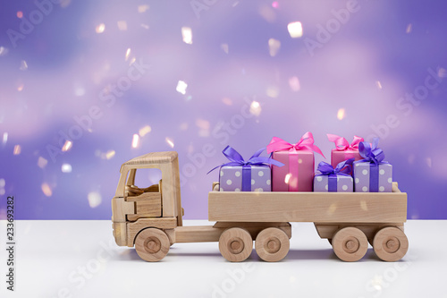 Boxes with gifts in purple with white polka dots and pink paper, carrying toy wooden truck.