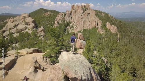 A Man Stands on a Rocky Peak Gazing Out to an Epic View of the Crags in Colorado, Aerial Orbiting Shot