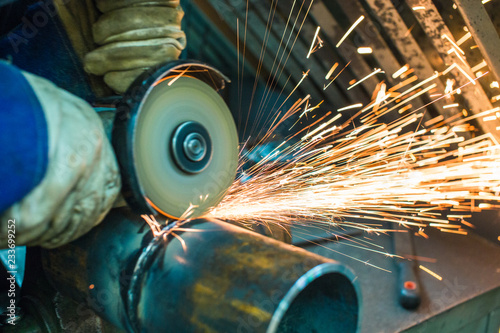 mechanic cleans a welded seam on a section of a steel pipe with the help of a grinding machine in the metal workshop