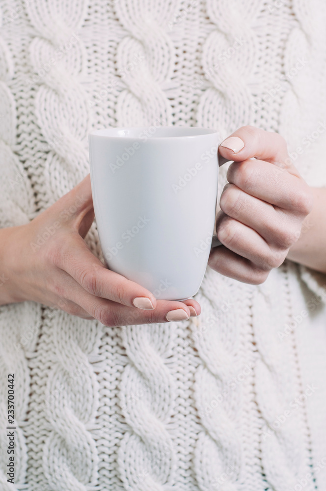 A woman in a white sweater holding a white mug in her hands. Template for text or design A woman in a white sweater holding a white mug in her hands. Template for text or design