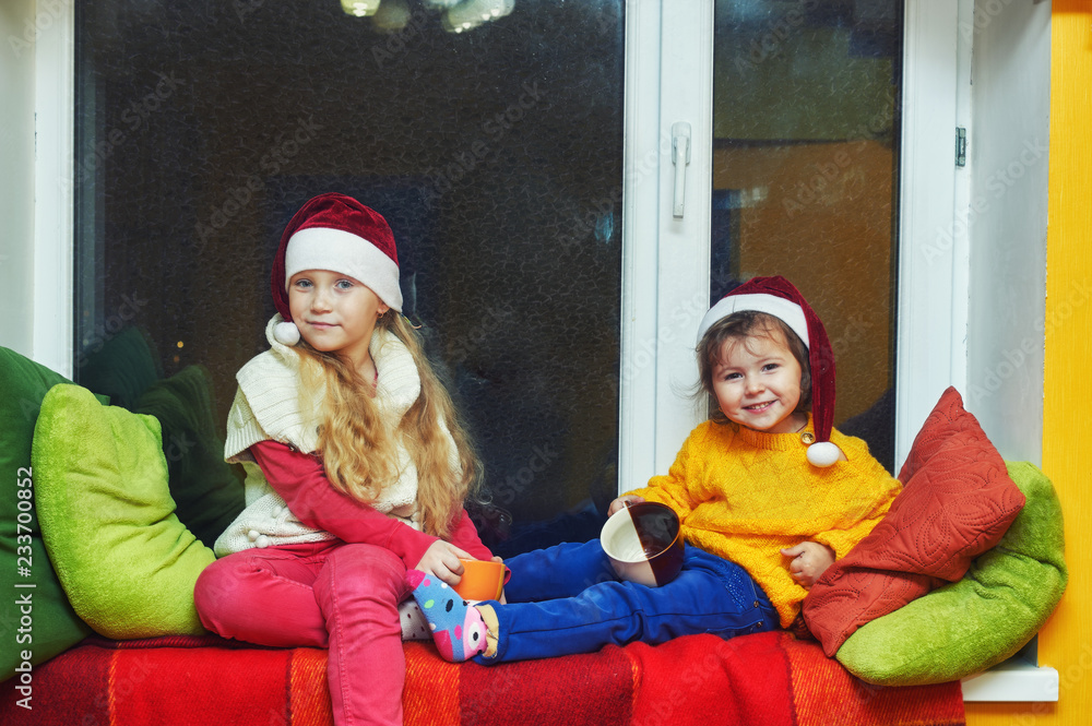 Fototapeta premium Pretty little girl in Christmas hats Santa in the house in anticipation of Christmas