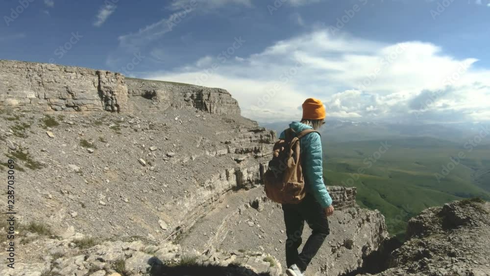 A girl with a backpack walks in nature on a plateau near a high precipice. Travel concept A girl with a backpack walks in nature on a plateau near a high precipice. Travel concept
