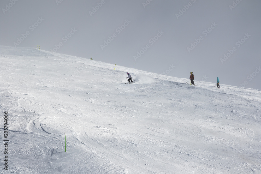 Skiers downhill on ski slope and sky in fog at gray winter day