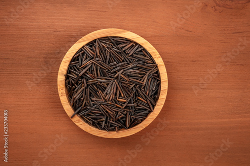 Black wild rice, shot from above in a wooden bowl on a dark rustic background with a place for text