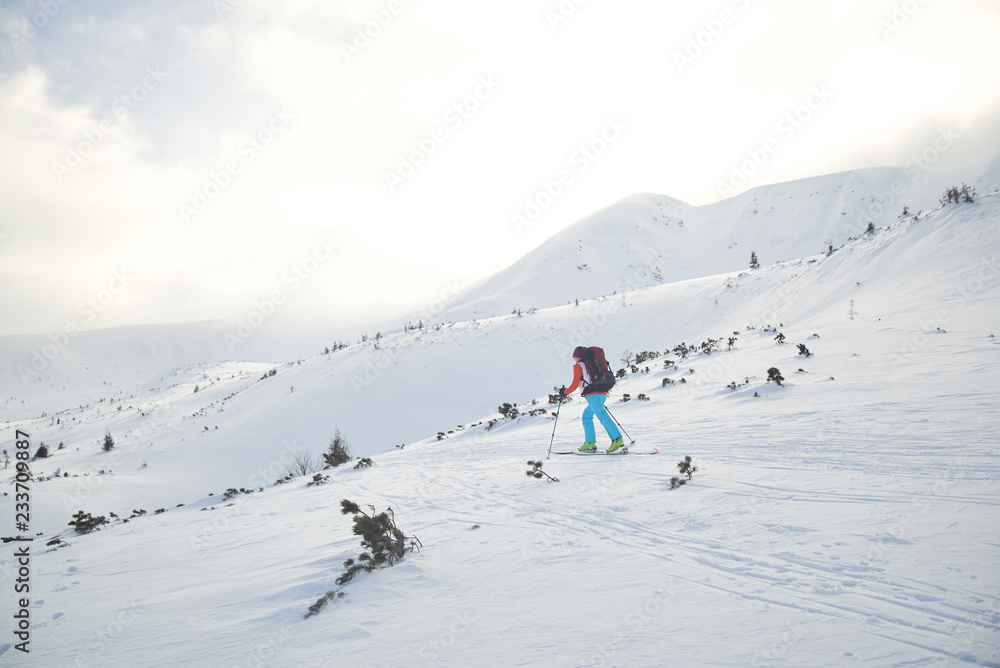Ski touring hiking alone up a summit in the winter mountains
