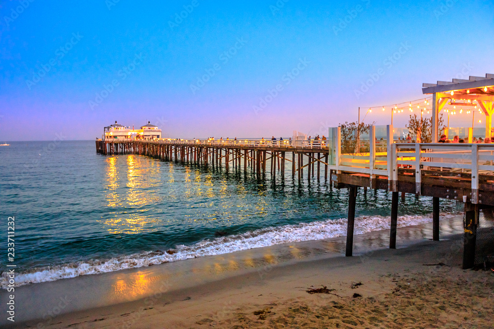 Naklejka premium Malibu Pier w Malibu, Kalifornia, Stany Zjednoczone, widok z Carbon Beach, malowniczy nadmorski krajobraz oświetlony nocą. Molo Malibu to historyczny punkt orientacyjny. Ujęcie niebieskiej godziny. Skopiuj miejsce.