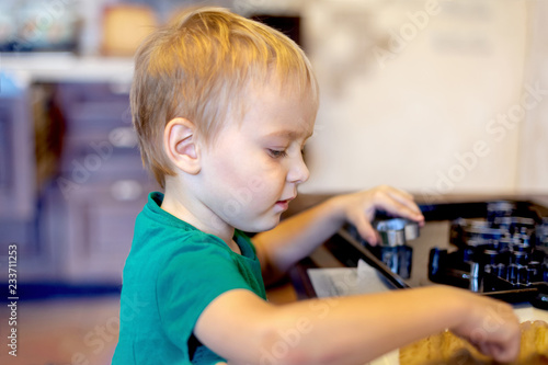 Cute caucasian baby boy helps in kitchen, making coockies. Casual lifestyle in home interior, pretty child alone. Indoors, copy space.