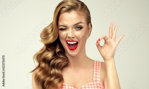 Pin-up retro girl with curly hair  winking, smiling and showing OK sign . Presenting your product. Expressive facial expressions
 photo