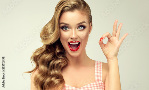 Pin-up retro girl with curly hair winking, smiling and showing OK sign . Presenting your product. Expressive facial expressions 