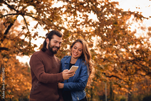 Young couple using cellphone in autumn colored park.