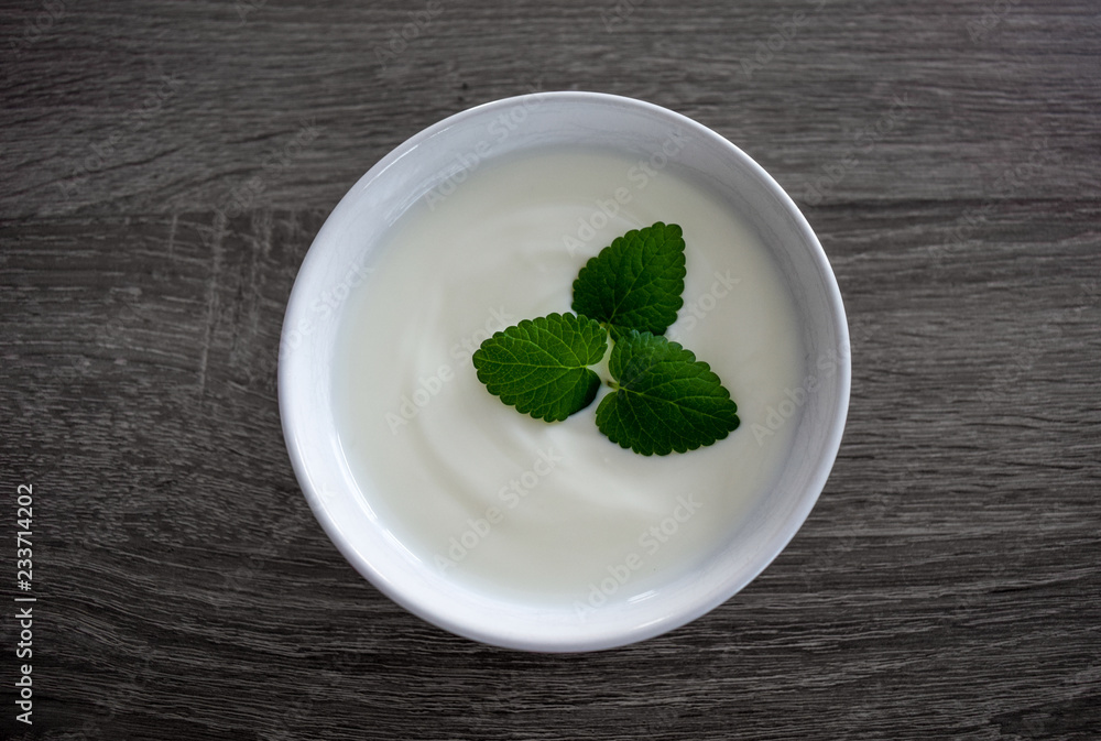 Ceramic bowl with white plain yogurt and mint leaves isolated on dark wooden background from above Ceramic bowl with white plain yogurt and mint leaves isolated on dark wooden background from above
