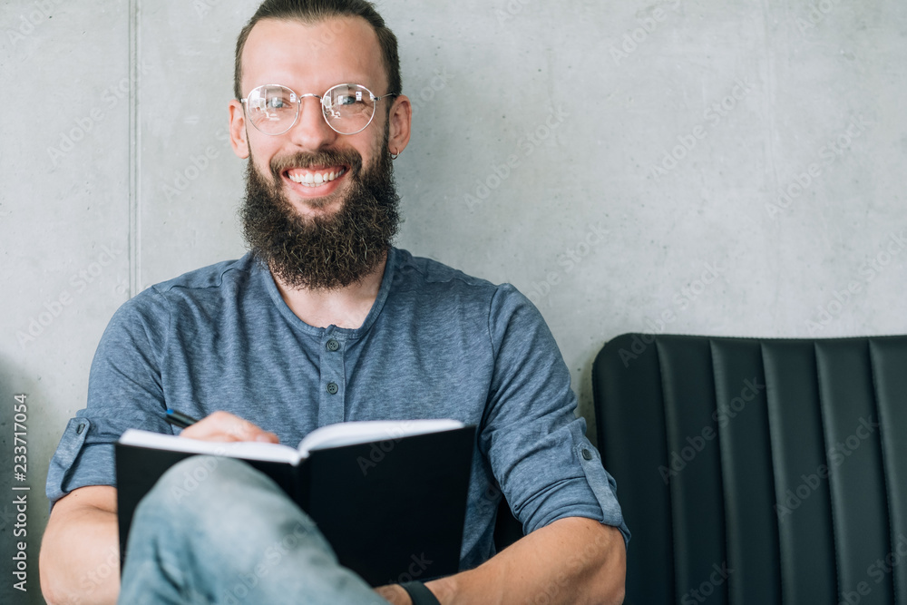 smiling bearded man in glasses with notepad in his hands. student education or training courses concept.