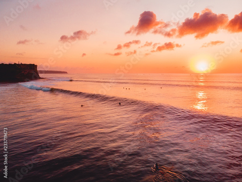 Aerial view of ocean with waves, surfers and warm sunset. Drone shot in Bali