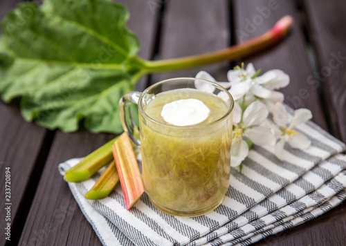 Sweet and sour kissel or kisel dessert made of an rhubarb (Rheum rhabarbarum) with the spash of whipped cream in a clear cup on a wooden background. Traditional dessert in Estonia, popular in spring. photo