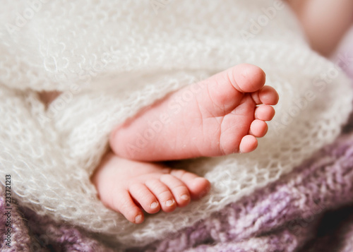 Close up of a tiny pink newborn baby toes feet, wrapped in a white soft knitted blanket.